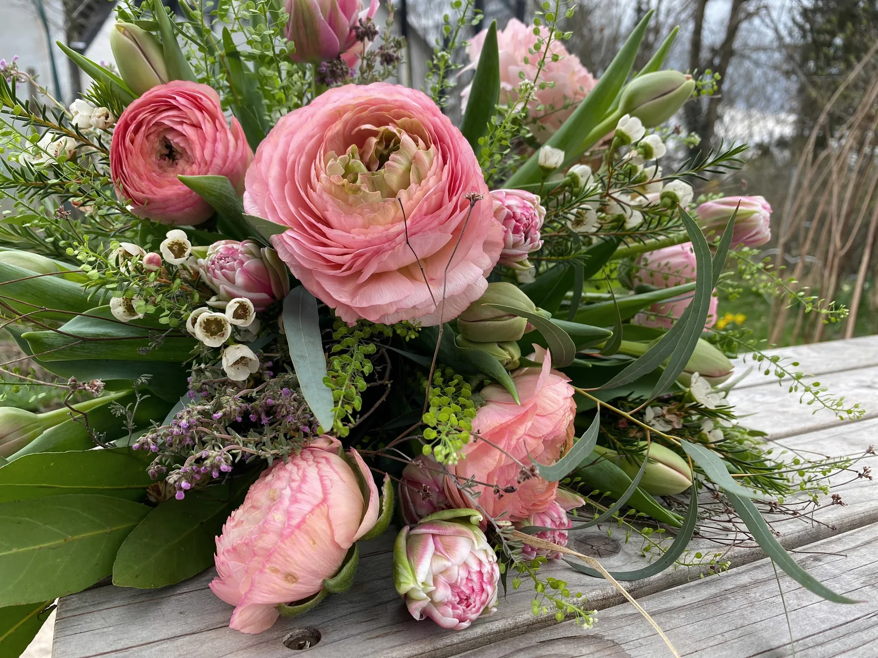 Locker arrangierter Strauß aus rosa Ranunkeln und Blüten auf Holz