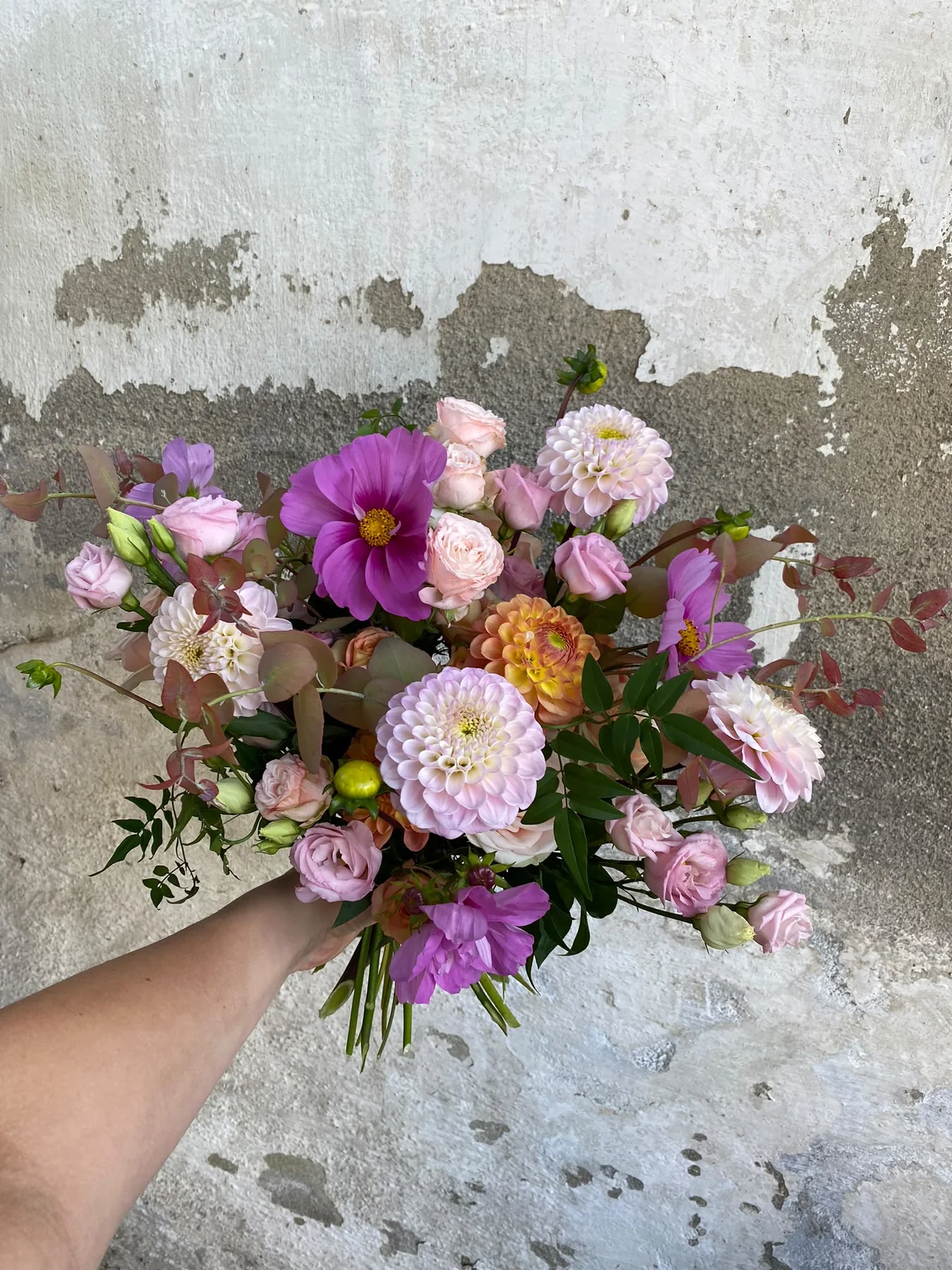 Handgebundener Strauß in Rosa und Violett vor einer hellen Wand